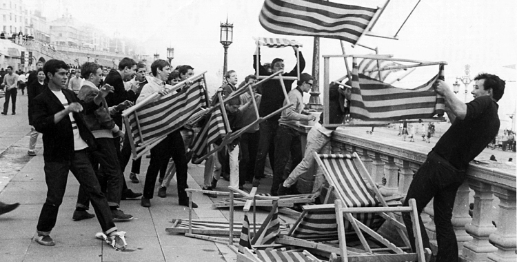 Argus Looking Back Series LB-25 Image of mods and rockers on Brighton Seafront during May 1964.  Group of Mods pictured throwing deckchairs fron the roof terrace of Brighton Aquarium on to Maderia Drive below.  Brighton Beach visible in background.